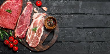 Çiğ et. Sığır eti ve domuz eti biftek kesme tahtası üzerinde baharatlar ile. Siyah bir rustik arka planda.