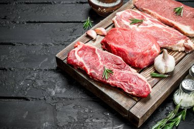 Çiğ et. Domuz ve sığır eti biftek bir tepsi ile baharat ve biberiye delikanlı. Siyah bir rustik arka planda.