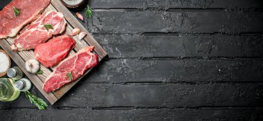 Çiğ et. Domuz ve sığır eti biftek bir tepsi ile baharat ve biberiye delikanlı. Siyah bir rustik arka planda.