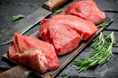 Çiğ et. Balta ve biberiye dalları ile sığır eti parçaları. Siyah bir rustik arka planda.