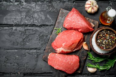 Çiğ et. Baharat ve otlar ile sığır eti parçaları. Siyah bir rustik arka planda.
