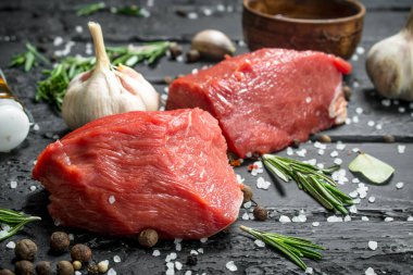 Çiğ et. Baharat ve otlar ile sığır eti parçaları bir ahşap tahta üzerine dilimlenmiş. Siyah bir rustik arka planda.