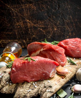 Çiğ et. Baharat, sarımsak ve biberiye ile taze et parçaları. Ahşap bir arka plan üzerinde.