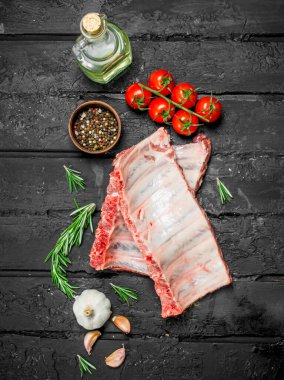 Domates ve baharat ile ham kaburga. Siyah bir rustik arka planda.