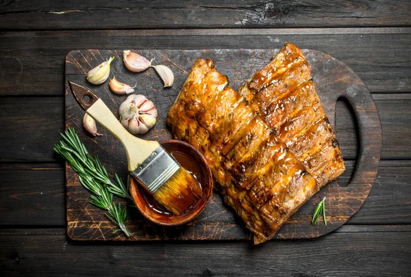 stock image Grilled ribs with sauce, herbs and spices. On a wooden background.