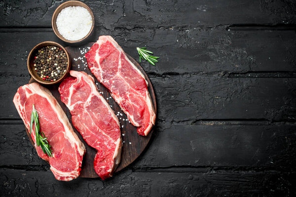 Raw beef steaks with spices. On a black rustic background.