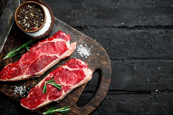 Raw beef steaks with spices. On a black rustic background.