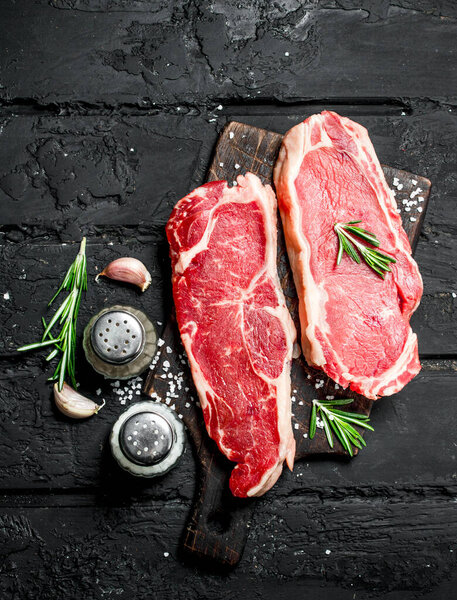 Raw beef steaks with spices and salt. On a black rustic background.