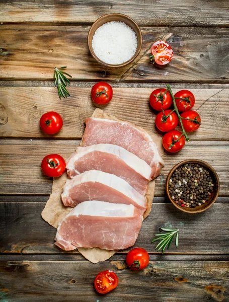 stock image Raw pork steaks with tomatoes and rosemary. On a wooden background.