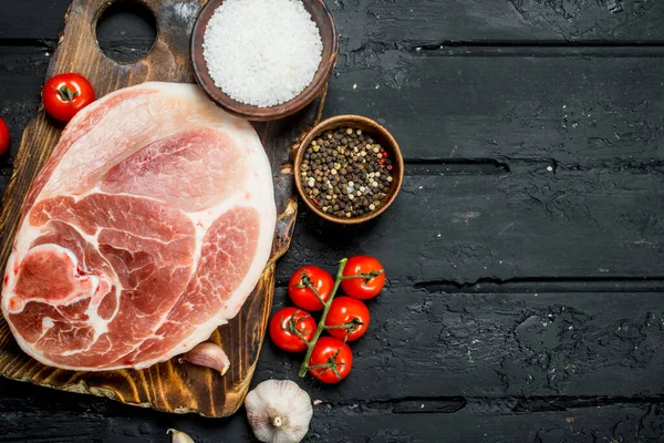 stock image Big raw pork steak with tomatoes and spices. On a black rustic background.