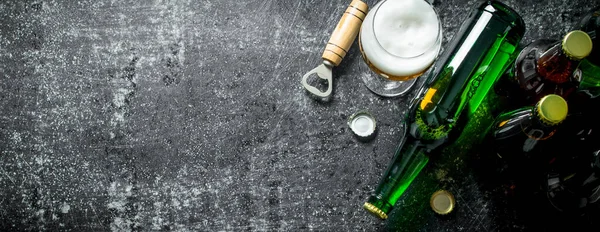 stock image Beer in a glass and a glass bottle with opener. On rustic background