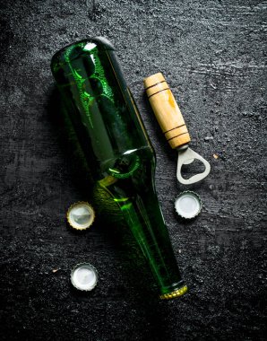 Açacağı ve kapakları ile cam bir şişe de Bira. Siyah rustik arka plan üzerinde