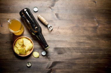 Şişede bira ve cips ve açacağı olan bir bardak. Ahşap arka planda