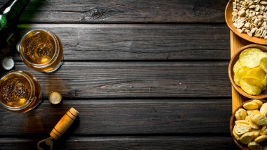 Bardakta bira ve çeşitli atıştırmalıklar. Siyah ahşap arka plan üzerinde