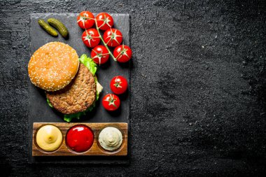 Bir dal üzerinde soslar ve domates ile bir taş Tahta burger. Siyah rustik arka plan üzerinde