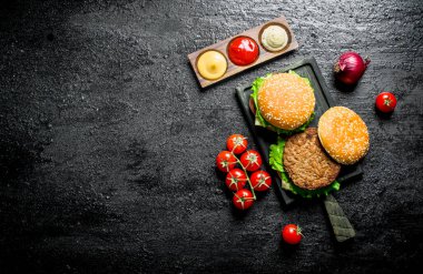 Domatesli, soslu ve soğanlı hamburgerler. Rustik arka planda