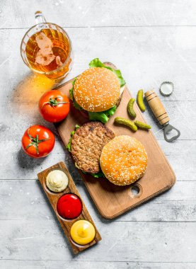 Biralı hamburgerler, domatesler ve farklı soslar. Beyaz ahşap arka plan üzerinde