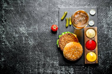 Bira, soslar ve gherkins ile Burger. Siyah rustik arka plan üzerinde