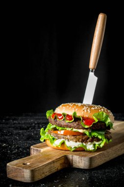 Bıçakla burger. Siyah rustik arka plan üzerinde