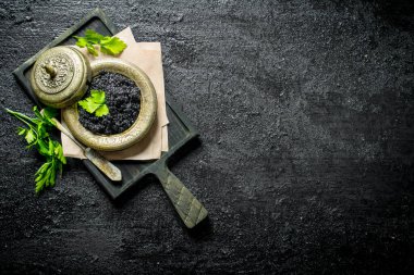 Maydanoz lu kesme tahtası üzerinde bir kapta siyah havyar. Siyah rustik arka plan üzerinde