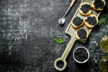 Siyah havyarlı sandviçler, bir kasede havyar ve beyaz şarap. Siyah rustik arka plan üzerinde