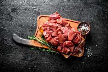 Baharat ve biberiye ile kesme Tahtası üzerinde Dilimlenmiş çiğ sığır eti. Siyah rustik arka plan üzerinde
