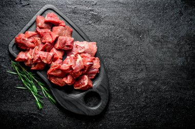 Biberiye ile siyah kesme Tahtası üzerinde dilimlenmiş çiğ sığır eti. Siyah rustik arka plan üzerinde
