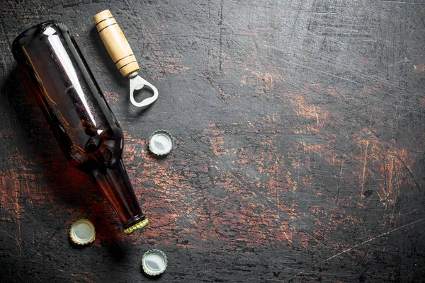 stock image Glass beer bottle and opener. On dark rustic background