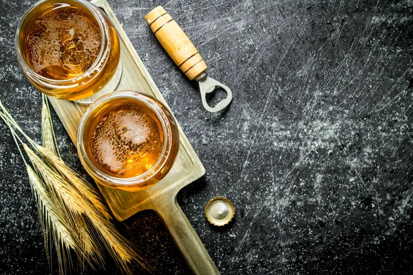 Stock image Two glasses of beer on a stand with spikelets and opener. On rustic background