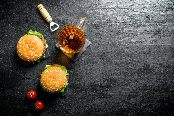Burgers with beer in a glass and tomatoes. On black rustic background