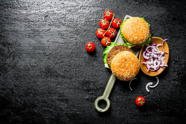 Burgers with chopped onions in bowl and cherry. On black rustic background