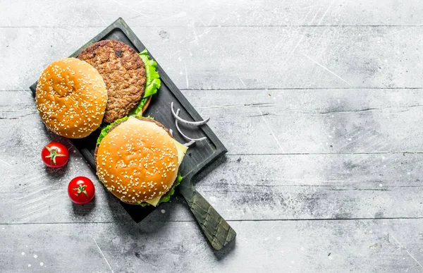 玉ねぎのスライスとトマトの黒い切り板のハンバーガー 白い木製の背景に — ストック写真