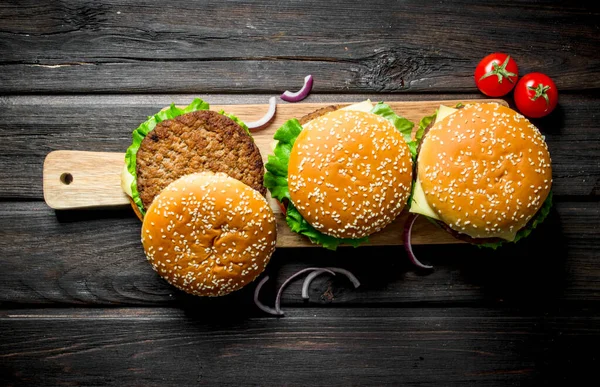 玉ねぎのスライスと木製のまな板上のハンバーガー 黒い木製の背景に — ストック写真