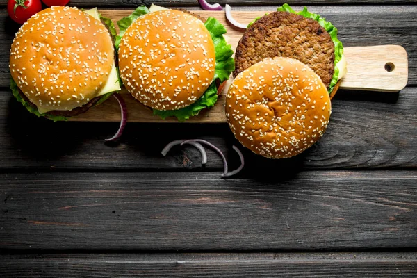 玉ねぎのスライスと木製のまな板上のハンバーガー 黒い木製の背景に — ストック写真