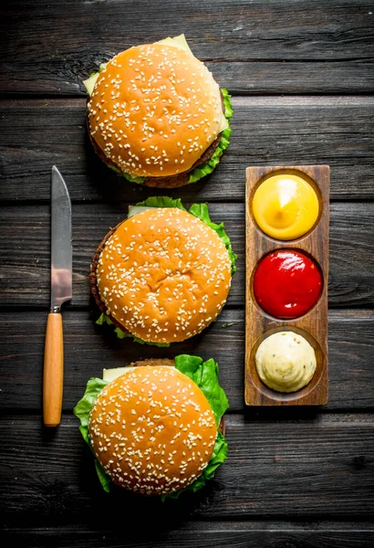 異なるソースとナイフを持つハンバーガー 黒い木製の背景に — ストック写真