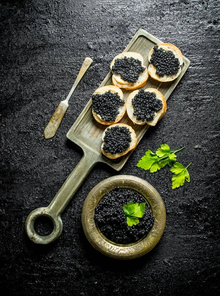 Sanduíches Com Caviar Preto Tábua Corte Fundo Rústico Preto — Fotografia de Stock