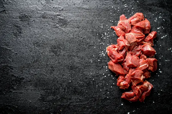 stock image Sliced raw beef with salt grains. On black rustic background