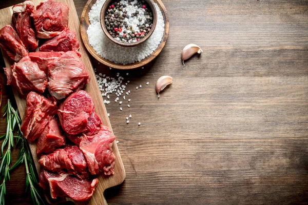 生の牛肉をニンニククローブ ローズマリー 調味料でボウルに入れます 木製の背景に — ストック写真