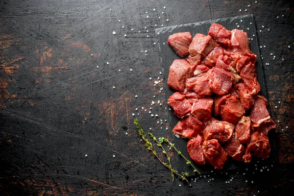 stock image Cut raw beef with thyme. On dark rustic background