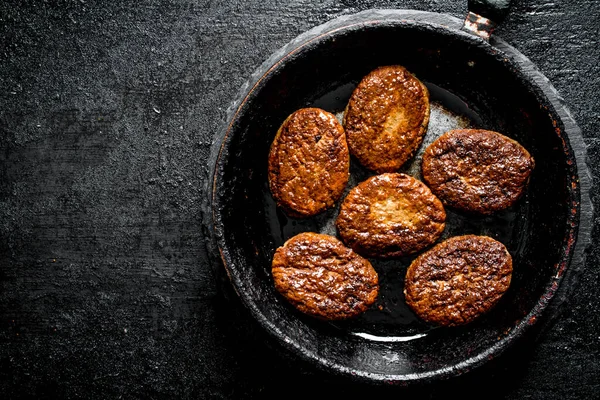 stock image Cutlets in an old pan. On black rustic background