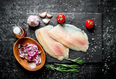 Kase, sarımsak ve biberiye doğranmış soğan ile Balık fileto. Siyah rustik arka plan üzerinde