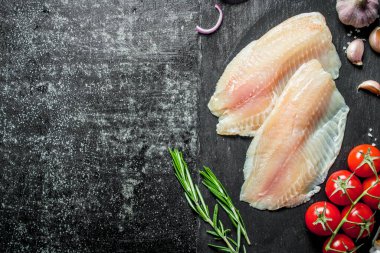 Bir dal, biberiye ve sarımsak karanfil domates ile Tilapia balık fileto. Siyah rustik arka plan üzerinde