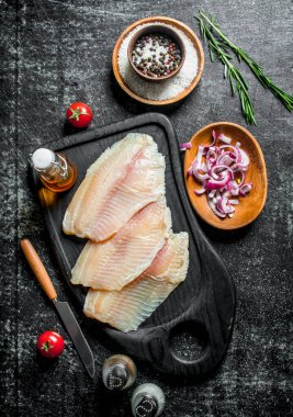 Kaselerde baharat ve soğan dilimleri ile Tilapia balık fileto. Siyah rustik arka plan üzerinde