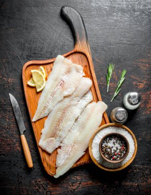 Limon, yağ ve baharat dilimleri ile bir kesme Tahtası üzerinde Balık fileto. Koyu rustik arka plan üzerinde