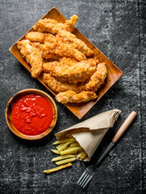 Patates kızartması ve soslu tavuk şeritleri. Koyu rustik arka plan üzerinde