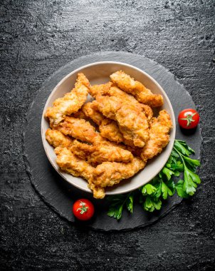 Maydanoz ve domates ile bir kapta Tavuk şeritler. Siyah rustik arka plan üzerinde