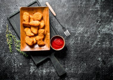 Kekik ve domates soslu kesme tahtasında tavuk nuggets. Koyu rustik arka plan üzerinde