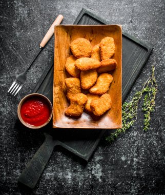 Kekik ve domates soslu kesme tahtasında tavuk nuggets. Koyu rustik arka plan üzerinde