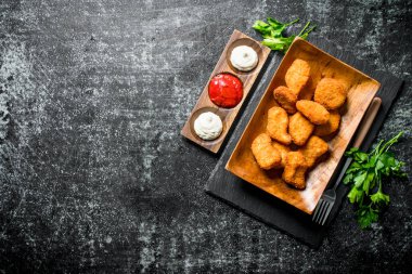 Yeşillik ve farklı soslar ile bir tabakta tavuk nuggets. Koyu rustik arka plan üzerinde