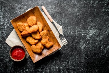 Bir kase kağıt ve domates sosu ile bir tabak ta tavuk nuggets. Koyu rustik arka plan üzerinde